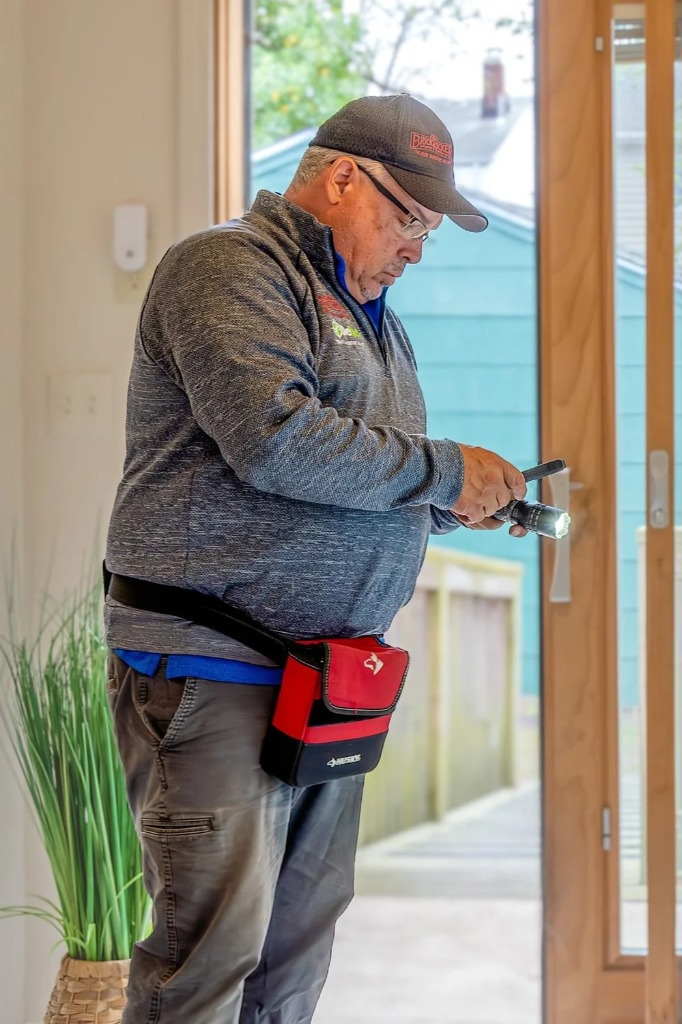 Inspector shining a hand light along an interior door frame and jamb during a home inspection